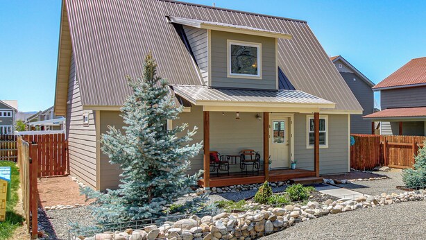 A two-story house with a covered patio, a small garden with rocks and plants, and a wooden fence. - 30 Mi to Crested Butte: Dog-Friendly Home By River (Gunnison)