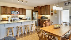 A kitchen with wooden cabinets, a stainless steel refrigerator, a dining table with chairs, and a bar stool area. - 30 Mi to Crested Butte: Dog-Friendly Home By River (Gunnison)