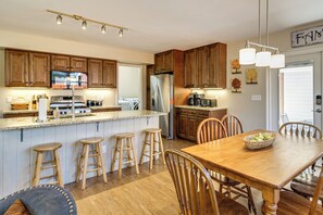Une cuisine avec des meubles en bois, un réfrigérateur en acier inoxydable, une table à manger avec des chaises et un coin bar avec des tabourets.