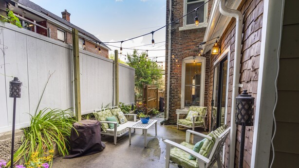 Une terrasse avec des meubles d’extérieur, un mur en briques et des guirlandes lumineuses.