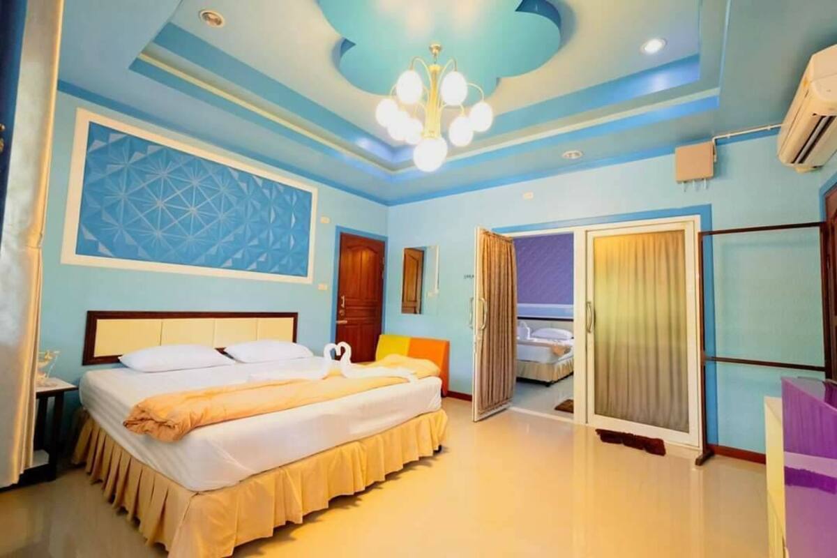 A hotel room with a bed, a chandelier, a door, and a window.