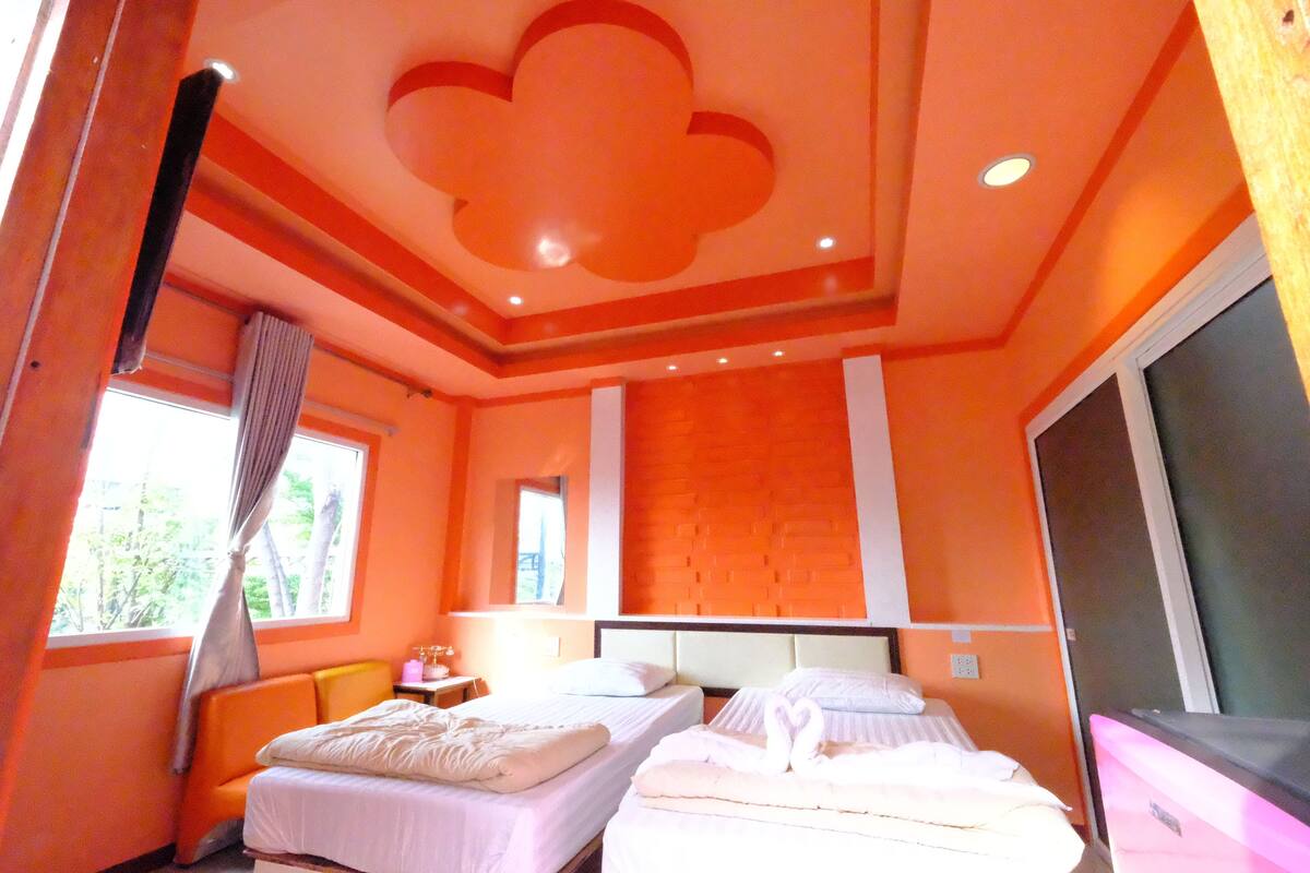 A hotel room with two beds, a large window with curtains, a TV, and a unique ceiling design.
