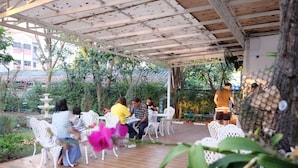 Un área de estar al aire libre con sillas y mesas blancas, rodeada de follaje y una fuente decorativa.