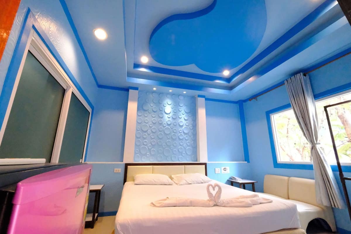 A room with a bed, a desk, a window with curtains, and a wall with a circular design.