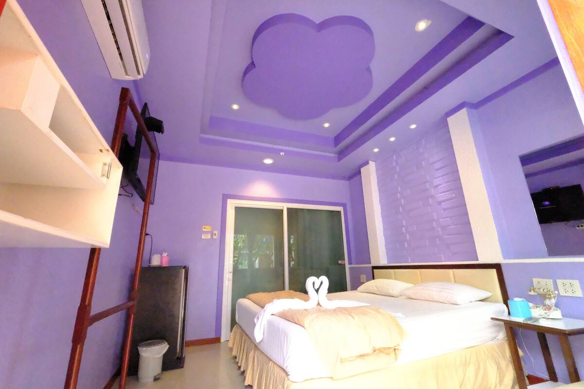 A bedroom with a bed, a dresser, a mirror, and a ceiling with a cloud design.