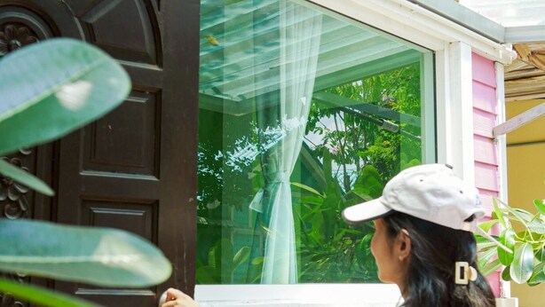 Una persona abre una puerta de madera oscura con diseños intrincados, que da paso a un espacio con vistas a la vegetación.