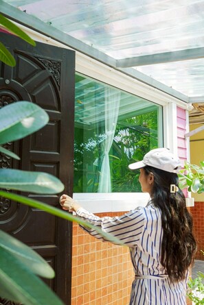 A person opening a dark wooden door with intricate designs, leading to a room with a view of greenery outside. - Rakkan Resort 2 (Nakhon Sawan)