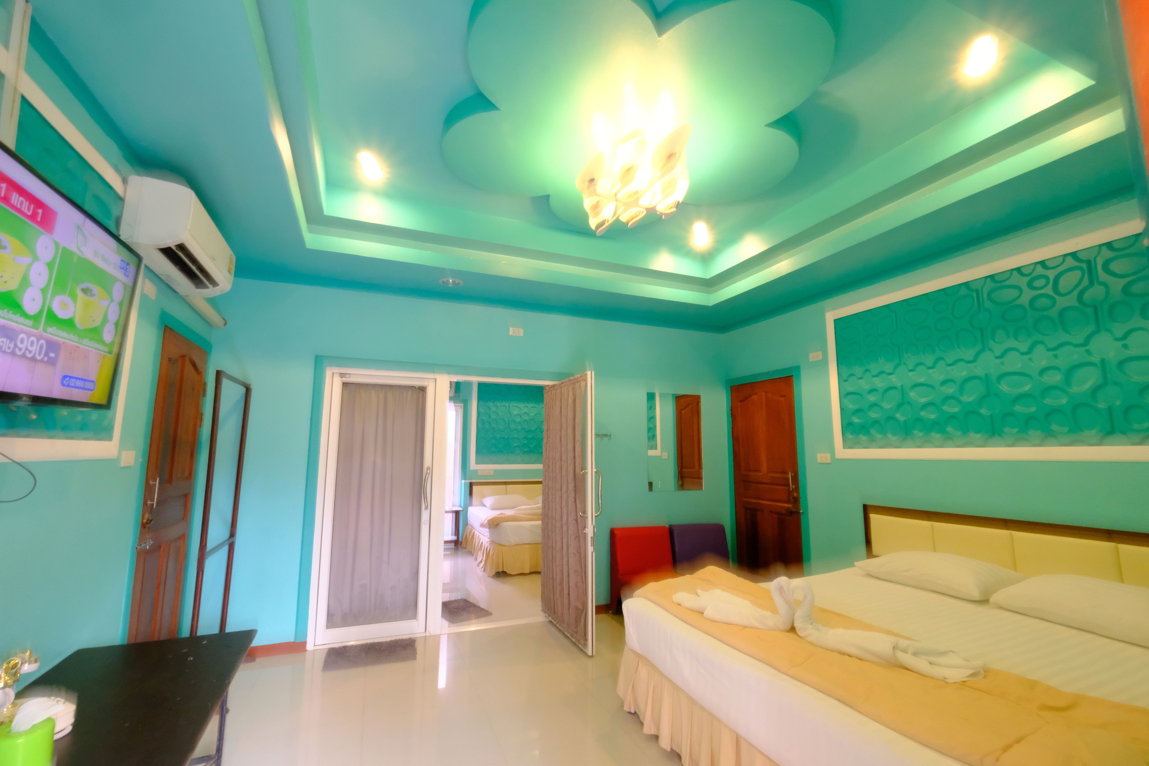 A hotel room with teal walls, a bed with white bedding, a ceiling light fixture, and a television on the wall.