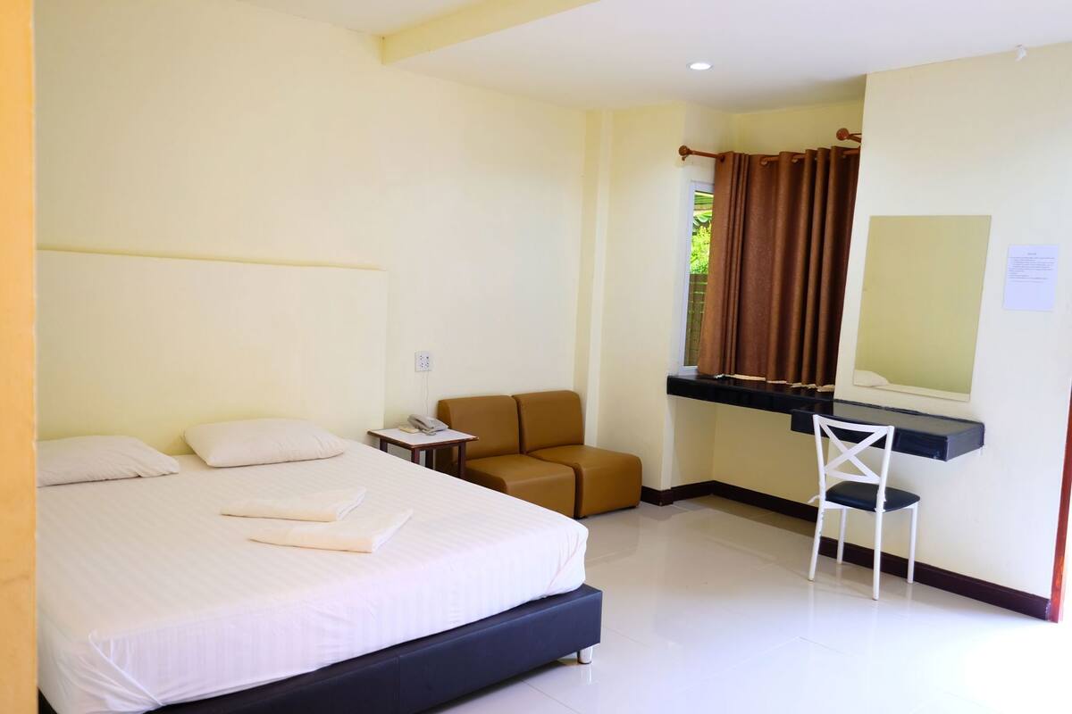 Habitación de hotel con cama, escritorio, silla, mesita y ventana con cortinas.