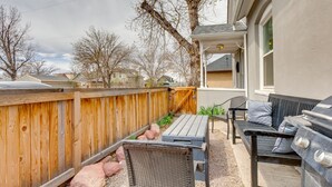 Un patio con una parrilla, mobiliario exterior y un cerco de madera.