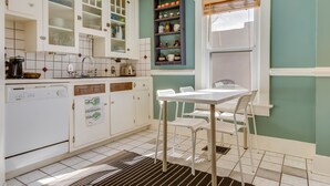 Una cocina con armarios blancos, una ventana con persianas y una zona de comedor con mesa y sillas.