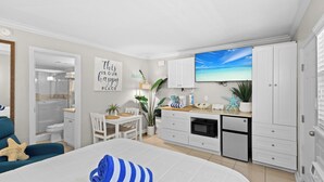 A modern bedroom with a large bed, a small desk, and a kitchenette.