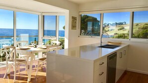 Une cuisine moderne dotée d’un grand îlot central, de meubles blancs et offrant une vue sur l’océan.