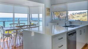 Une cuisine moderne dotée d’un grand îlot central, de meubles blancs et offrant une vue sur l’océan.