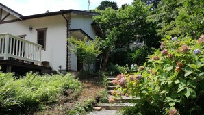 A white building with a balcony, surrounded by lush greenery and flowering plants. - kuu and fuu (Oshima)