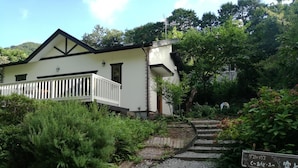 A house with a white exterior and a wooden deck. There is a garden with various plants and a gravel path leading to the house. - kuu and fuu (Oshima)