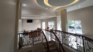 Um lobby espaçoso com uma escadaria moderna, uma TV de tela plana na parede e grandes janelas que permitem a entrada de luz natural.