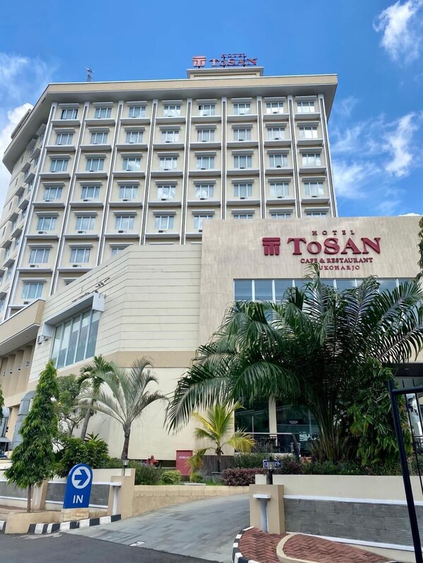 A hotel building with multiple floors, a prominent sign for 'Tosan Hotel', and a sign indicating the direction to the hotel entrance.