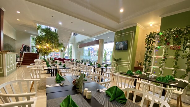 Um restaurante com cadeiras brancas, mesas escuras e guardanapos verdes.