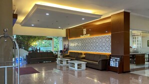 Um saguão de hotel com balcão de recepção, sofás, mesa de centro e escada que leva a um andar superior.