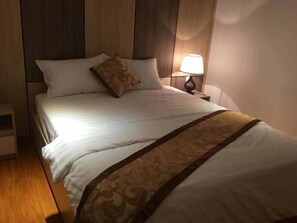 Una cama bien hecha con un cubrecolcha estampado, una lámpara de noche y un cabecero de madera.