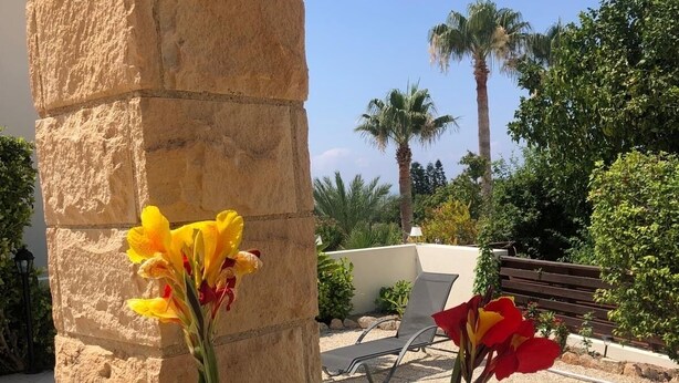 A stone pillar with flowers, a pool, and outdoor seating.