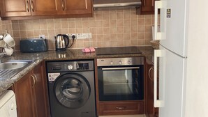 A compact kitchen with wooden cabinets, a built-in oven, a washing machine, and a toaster.