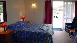 A hotel room with a bed, a desk, a chair, a lamp, and a view of the outside. - Raceway Motel (Christchurch)