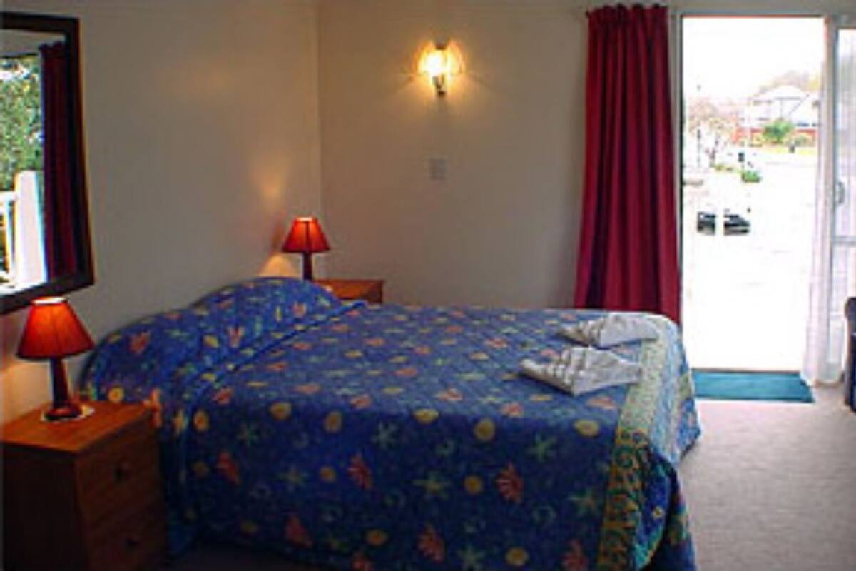 A hotel room with a bed, a desk, a chair, a lamp, and a view of the outside.