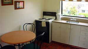 A small kitchen with a stove, sink, and a window. There is a table and two chairs. - Raceway Motel (Christchurch)