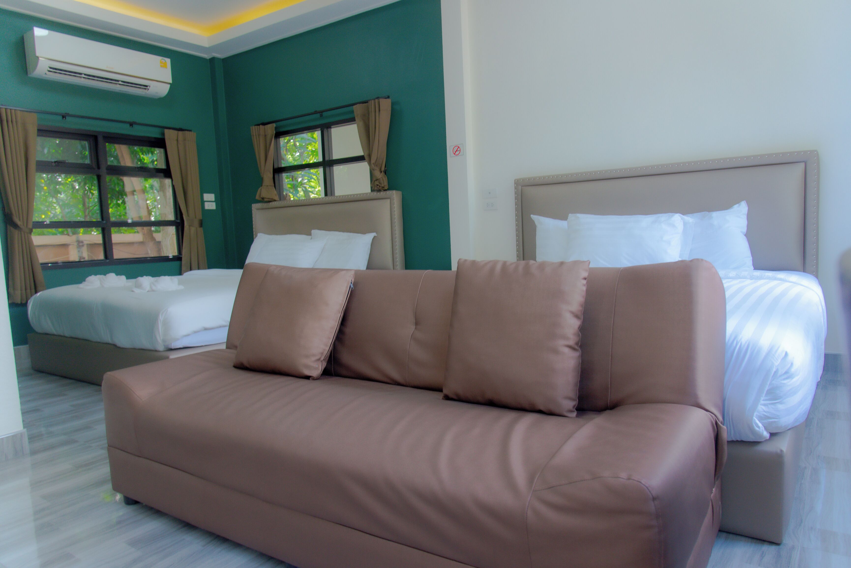 Quarto de hotel com sofá marrom, cama com roupa de cama branca e janela com cortinas.