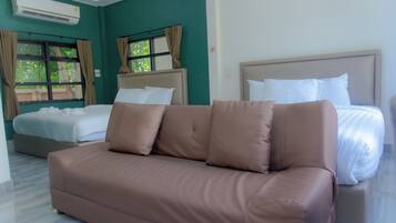 Quarto de hotel com sofá marrom, cama com roupa de cama branca e janela com cortinas.