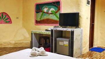 Habitación de hotel con cama, televisión, escritorio pequeño y un cuadro en la pared.