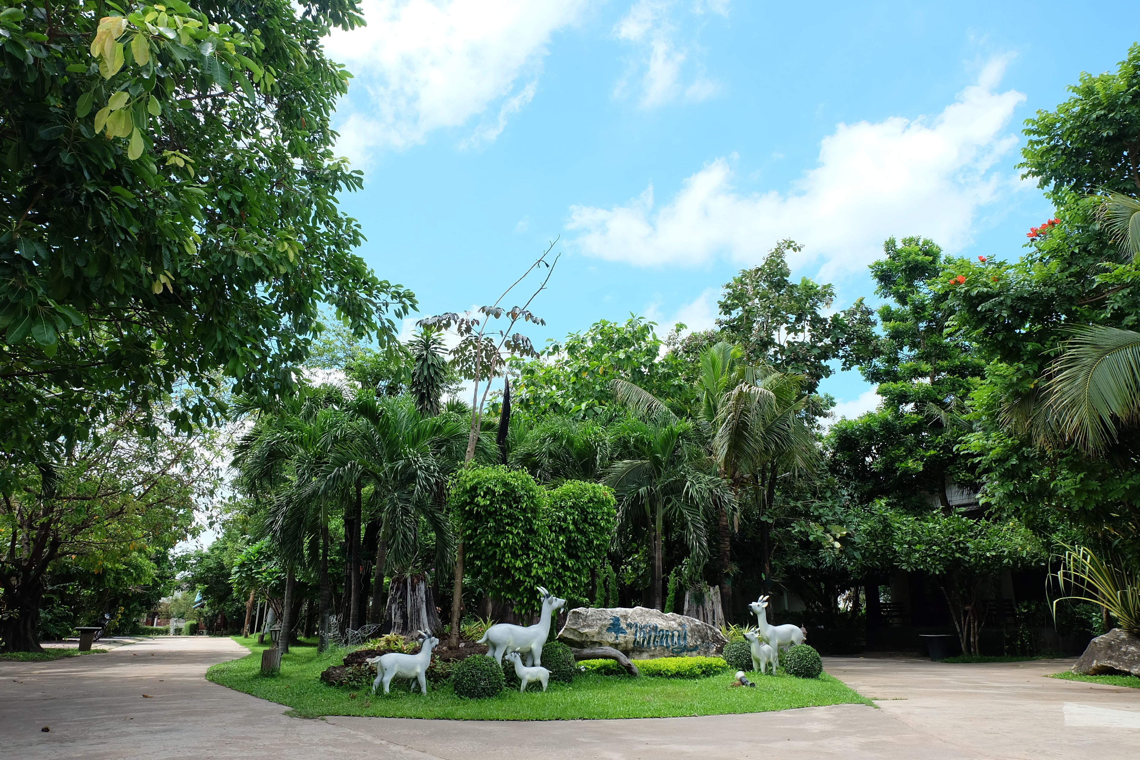 A park with a paved walkway, lush greenery, and white animal sculptures.
