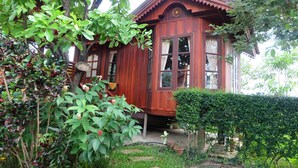 A wooden house with a porch, surrounded by lush greenery and a garden. - Big Tree Resort (Kamphaeng Phet)