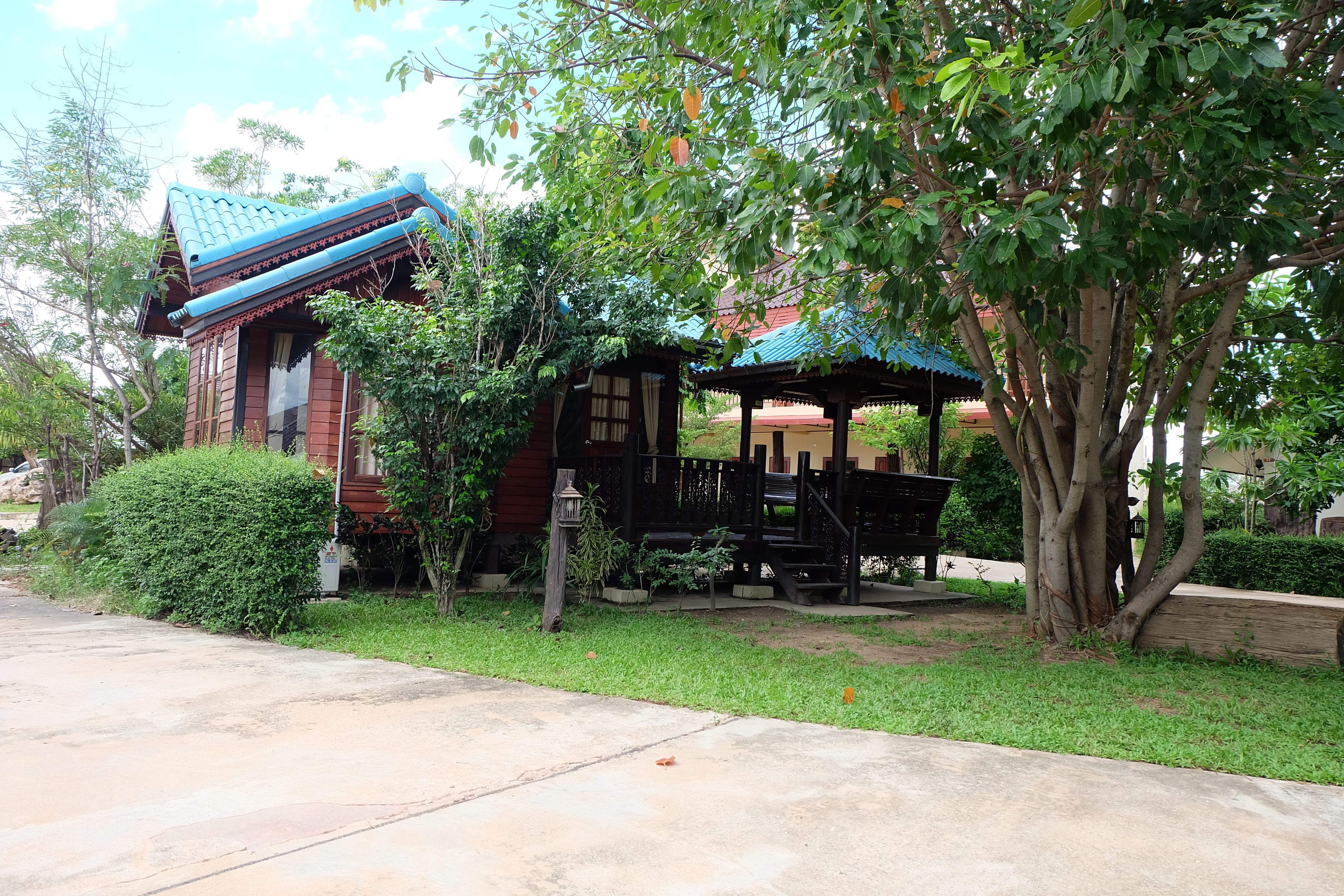 A traditional building with a tiled roof, a wooden structure with a roof, and a large tree in the foreground.