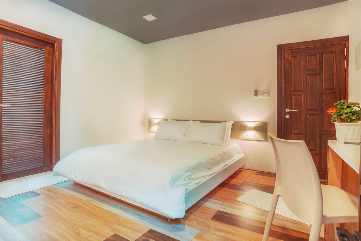 A bedroom with a bed, a chair, a wooden door, and a microwave.