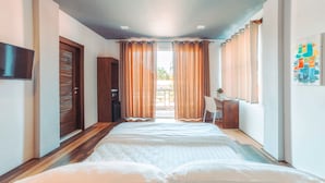 A hotel room with a bed, a desk, a chair, a TV, and a view of the outdoors.