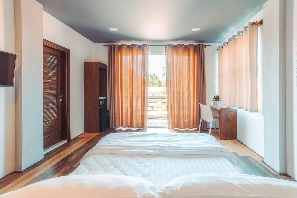 A hotel room with a bed, a desk, a chair, a TV, and a view of the outdoors.