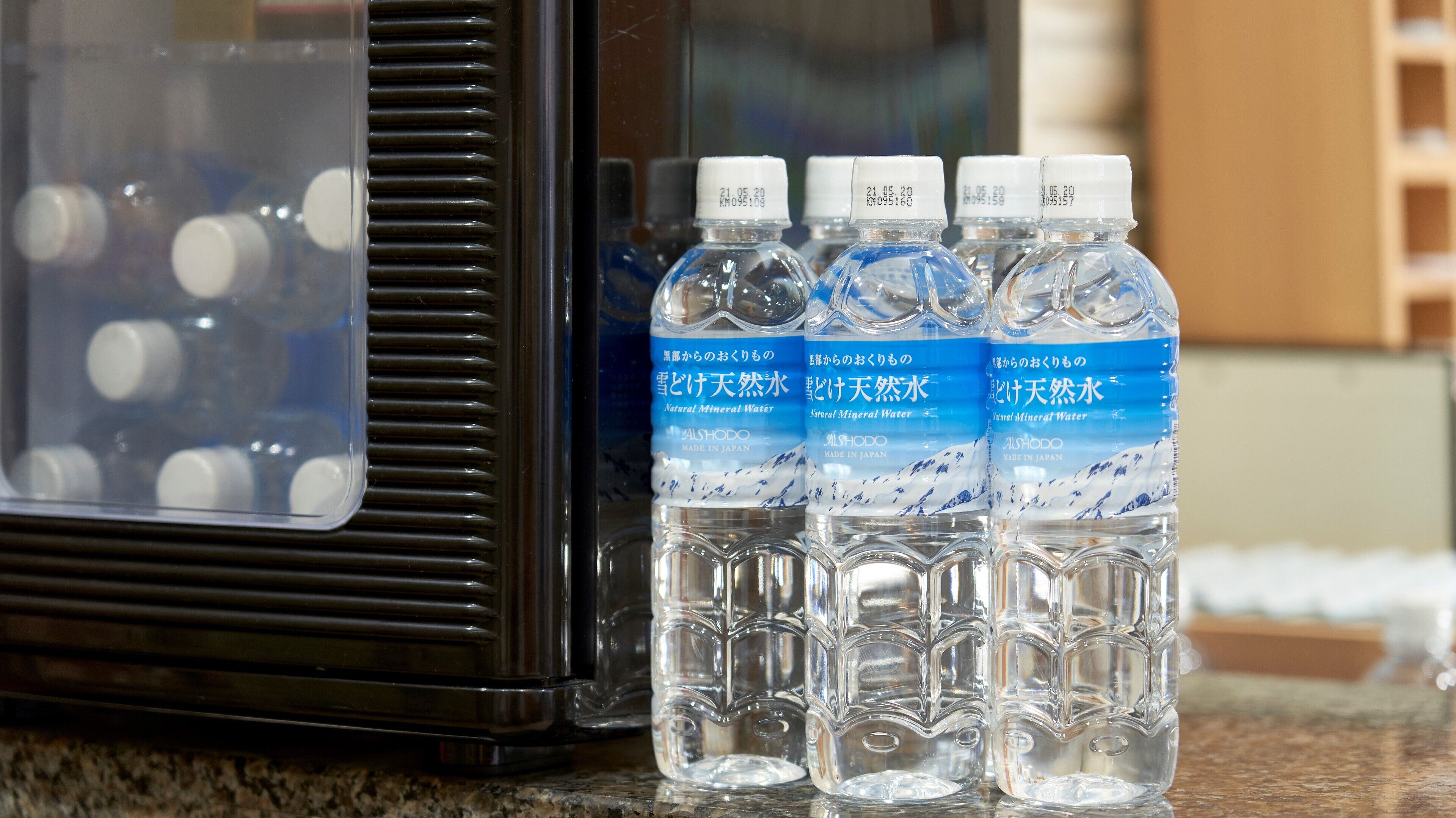 Cuatro botellas de agua mineral Alshodo sobre una encimera junto a un electrodoméstico negro.