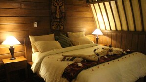 A wooden-paneled bedroom with two bedside lamps, a bed with white linens, and a decorative headboard. - Gili Lumbung Bungalow (Gili Air)