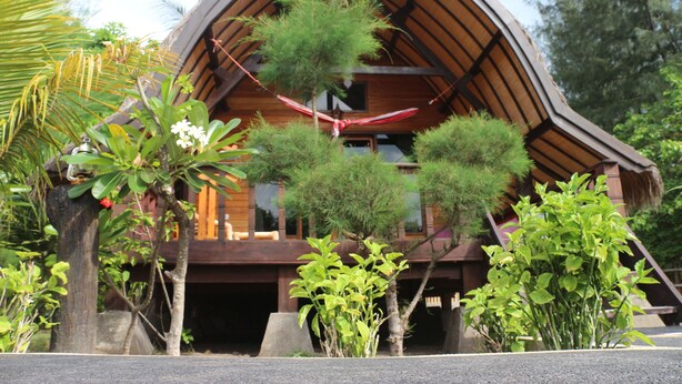 A wooden cabin with a sloped roof, surrounded by lush greenery and small trees. - Gili Lumbung Bungalow (Gili Air)