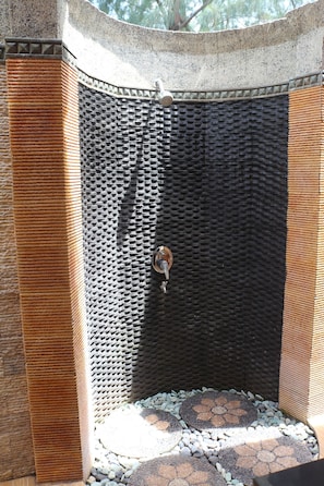 Box de chuveiro em pedra com parede texturizada e chuveiro de metal.