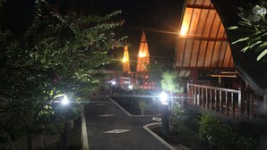 A nighttime view of a building with a distinctive triangular roof and a pathway leading to it. - Gili Lumbung Bungalow (Gili Air)