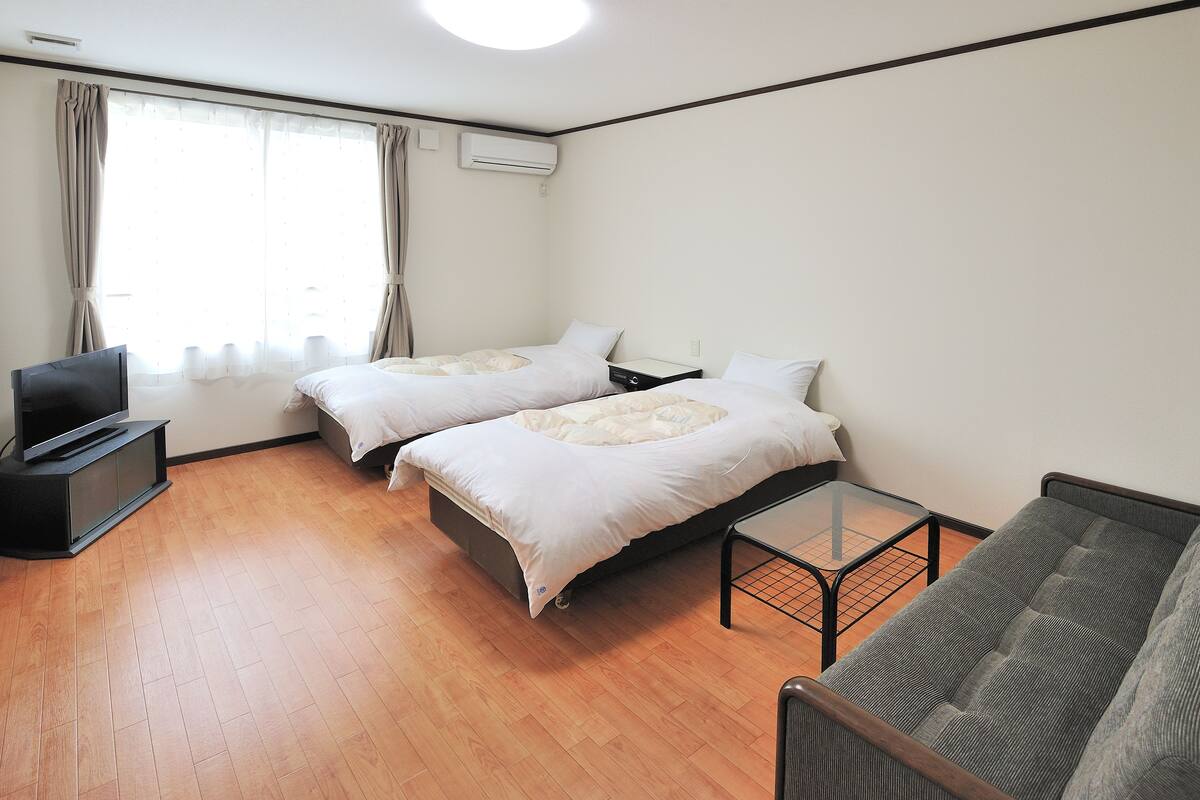 A hotel room with two beds, a TV, a small table, and a sofa.