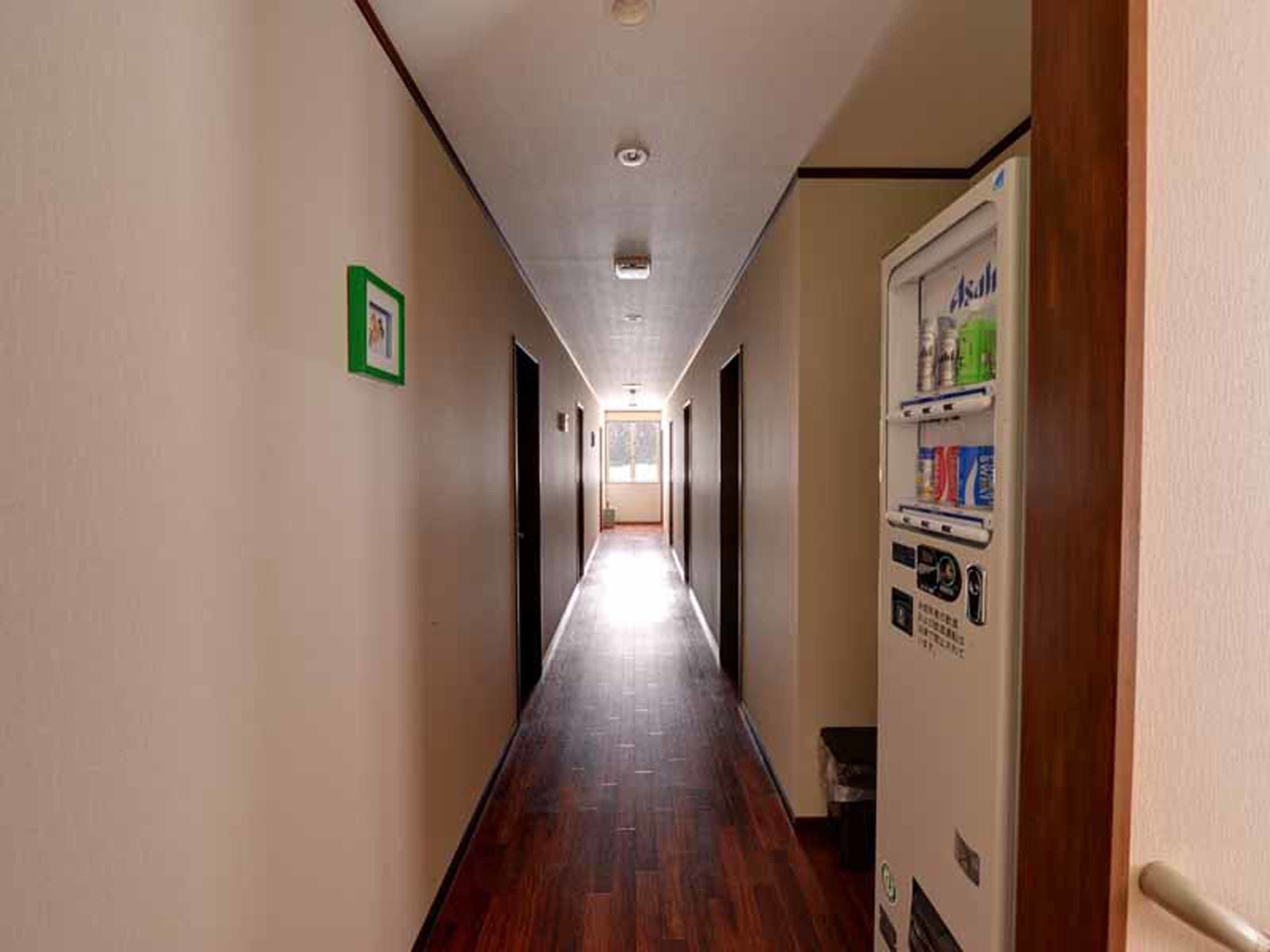 A long, narrow hallway with wooden flooring and a vending machine on the right.