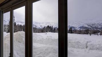 Vista a través de una ventana con un paisaje nevado, montañas y árboles.