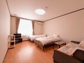 Camera d'albergo con due letti, televisione, scrivania e finestra con tende.