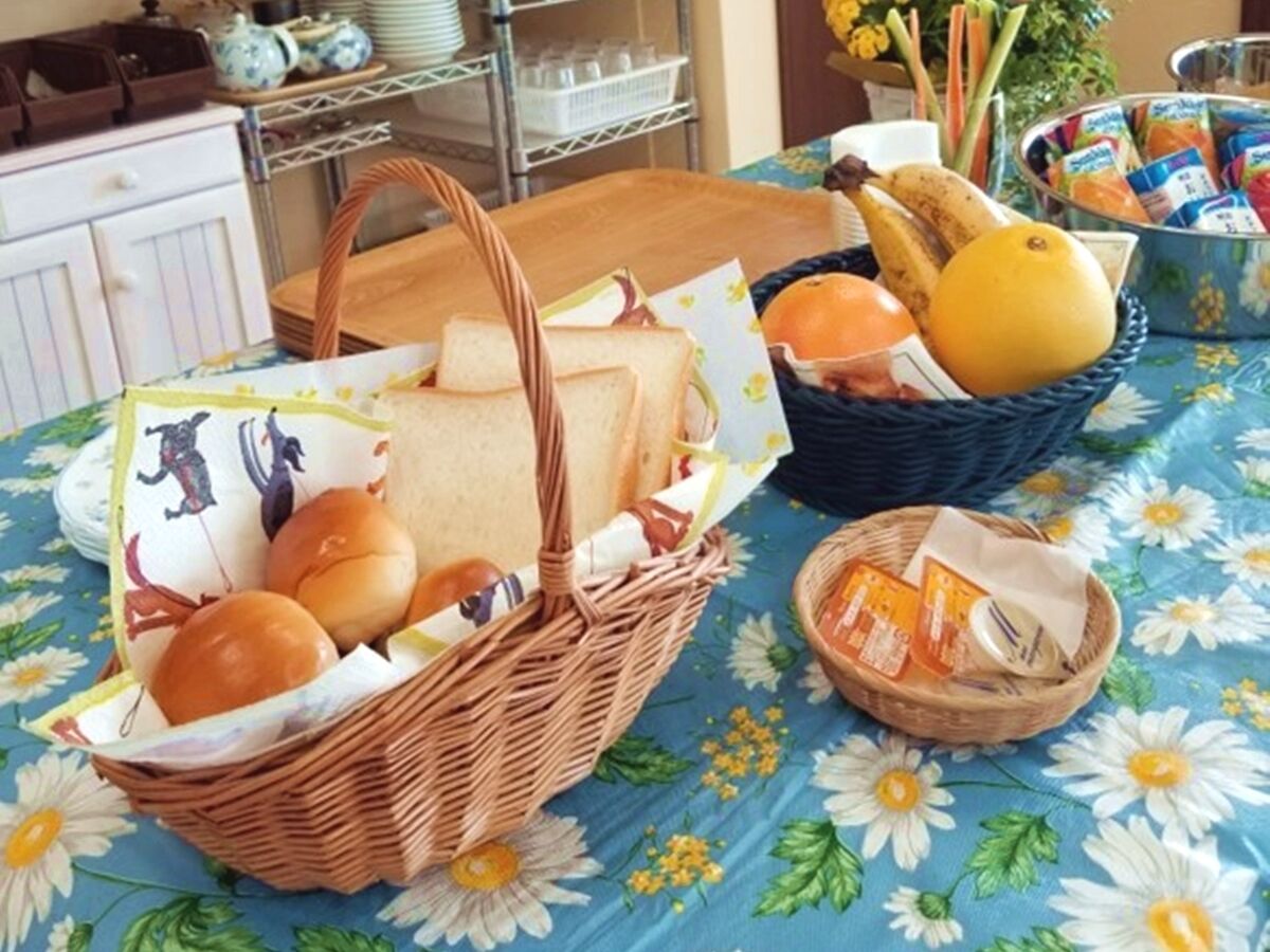 A table with a floral tablecloth, two wicker baskets containing bread and fruits, and a small basket with packaged snacks.