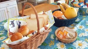 A table with a floral tablecloth, two wicker baskets containing bread and fruits, and a small basket with packaged snacks.
